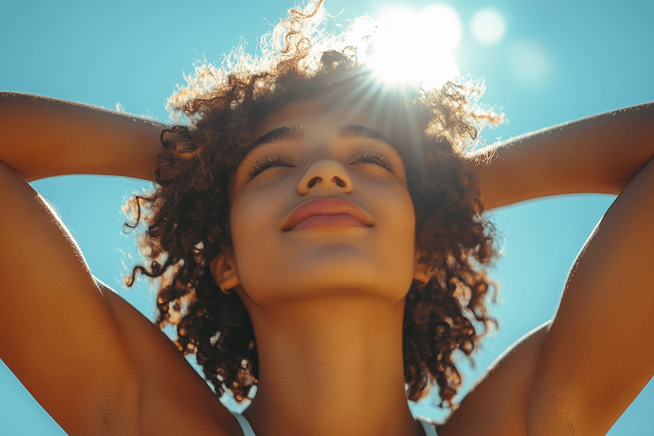 A woman with curly hair smiles as sunlight gently shines on her face, creating a warm and cheerful atmosphere.