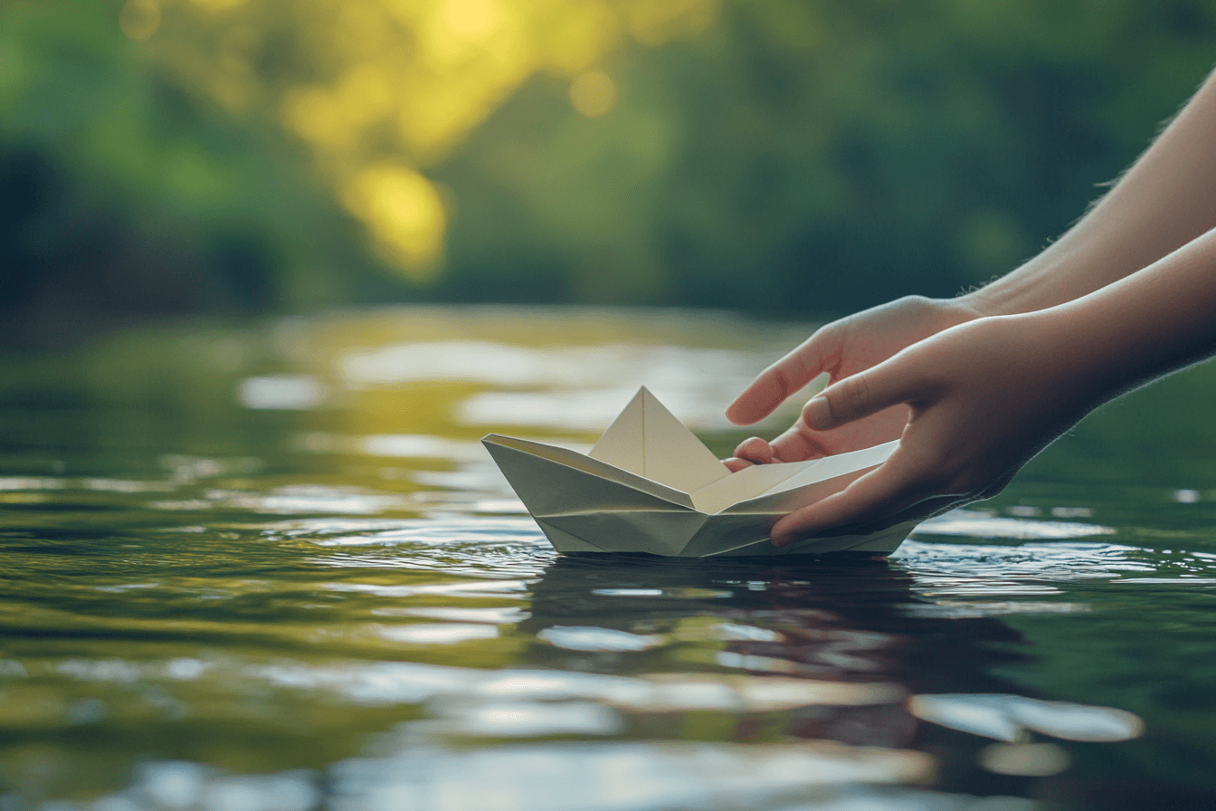 A person gently holds a paper boat above the water, ready to set it afloat.